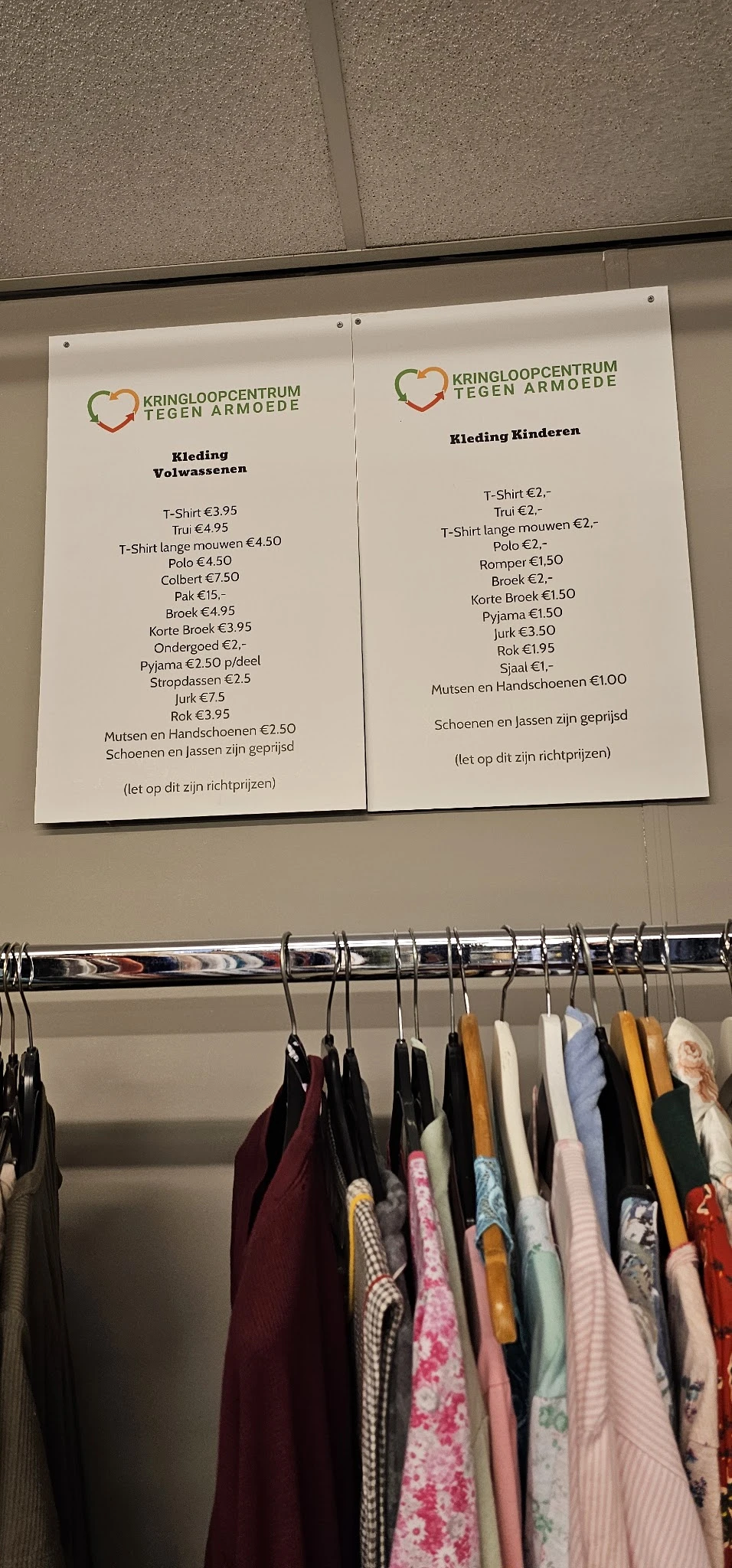 Prijslijst met kledingstukken en schoenen, onder een rek met hangers met kleding