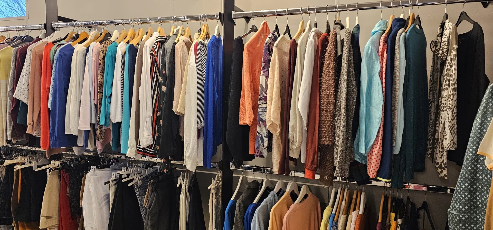 Rekken met tweedehands kleding in diverse kleuren en stijlen, met bovenrek voor jassen en onderrek voor broeken