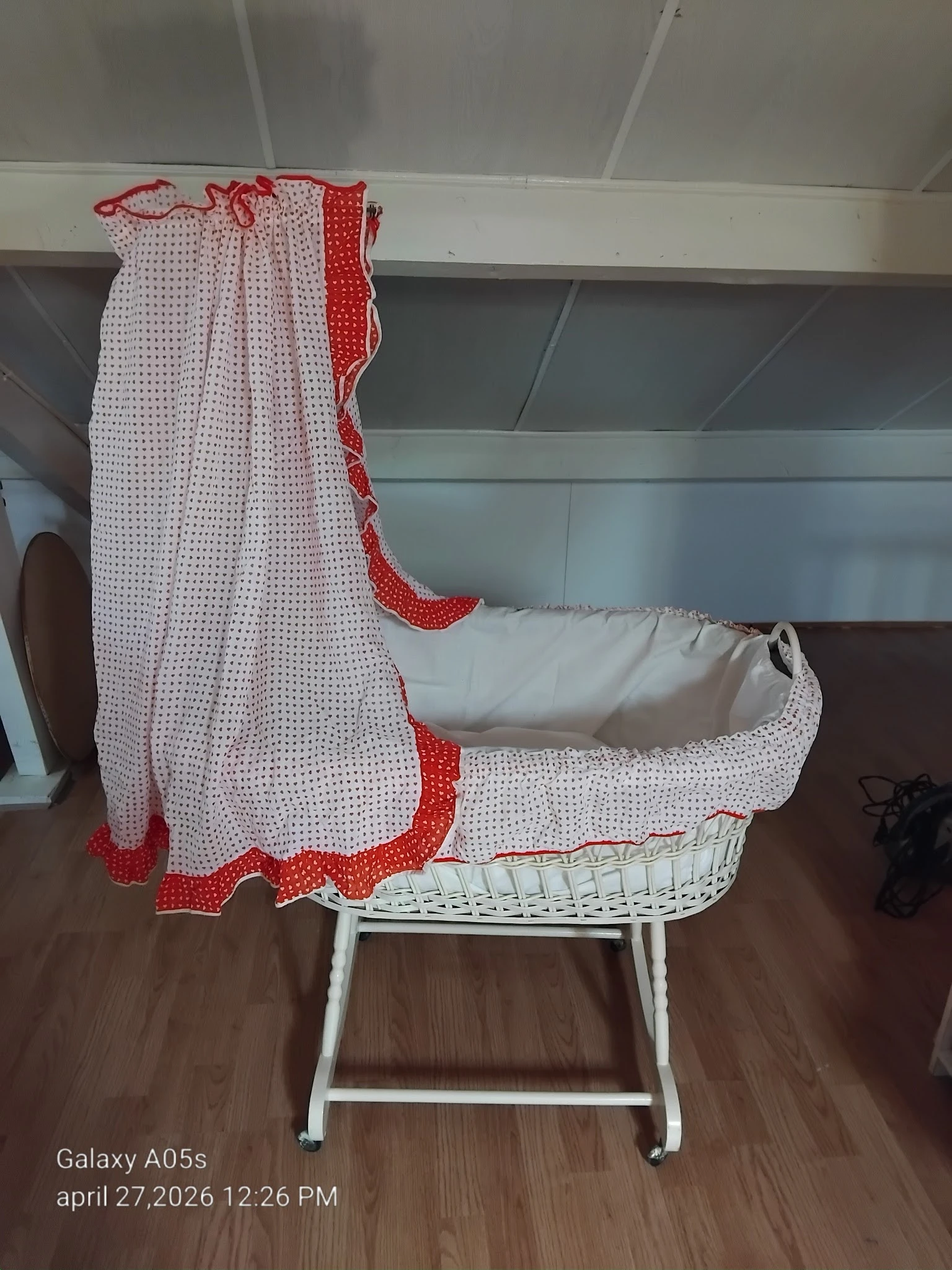 Vintage wiegje met rode en witte bedding en matras, staand op houten vloer