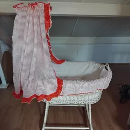 Vintage wiegje met rode en witte bedding en matras, staand op houten vloer