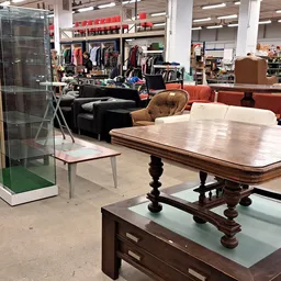 Winkelvloer met houten eettafel, bruine fauteuil, zwarte bank en displaykasten met kleding op achtergrond