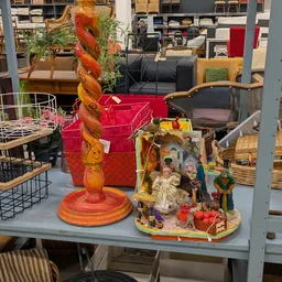 Uitgestalde decoratieve items in een kringloopwinkel: een houten spiraalvormig object, rode dozen, een kerststal en diverse h