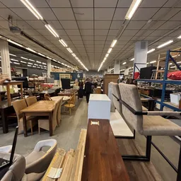 Ruim winkelbinnenruimte met uitgestalde meubels, tafels, stoelen en banken onder fluorescente verlichting