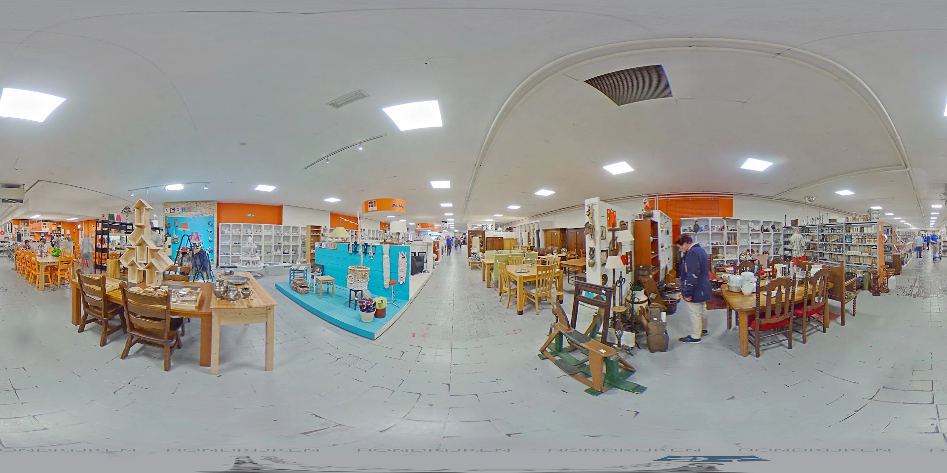Panoramafoto van de winkelvloer met diverse afdelingen, stellingen met artikelen, houten meubels en blauwe display-elemen aan
