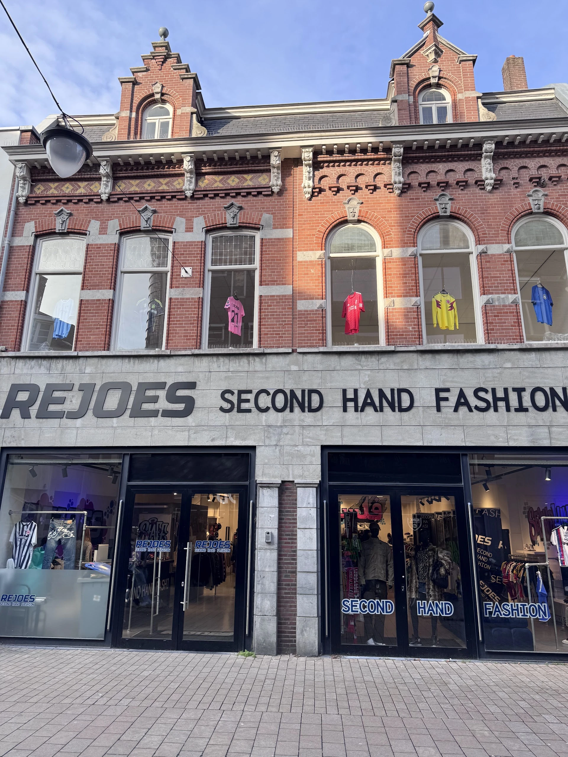 Gevel van tweedehandsmodeboetiek met uitstalkast vol gekleurde kleding en grote winkelnaam