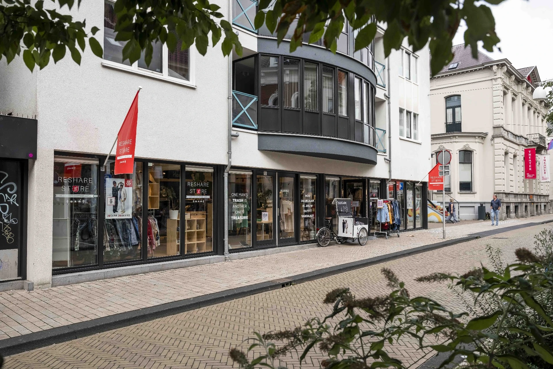 Gevel van kringloopwinkel aan Ceramstraat met zwarte pui, rode vlaggen en uitgestalde spullen in etalage