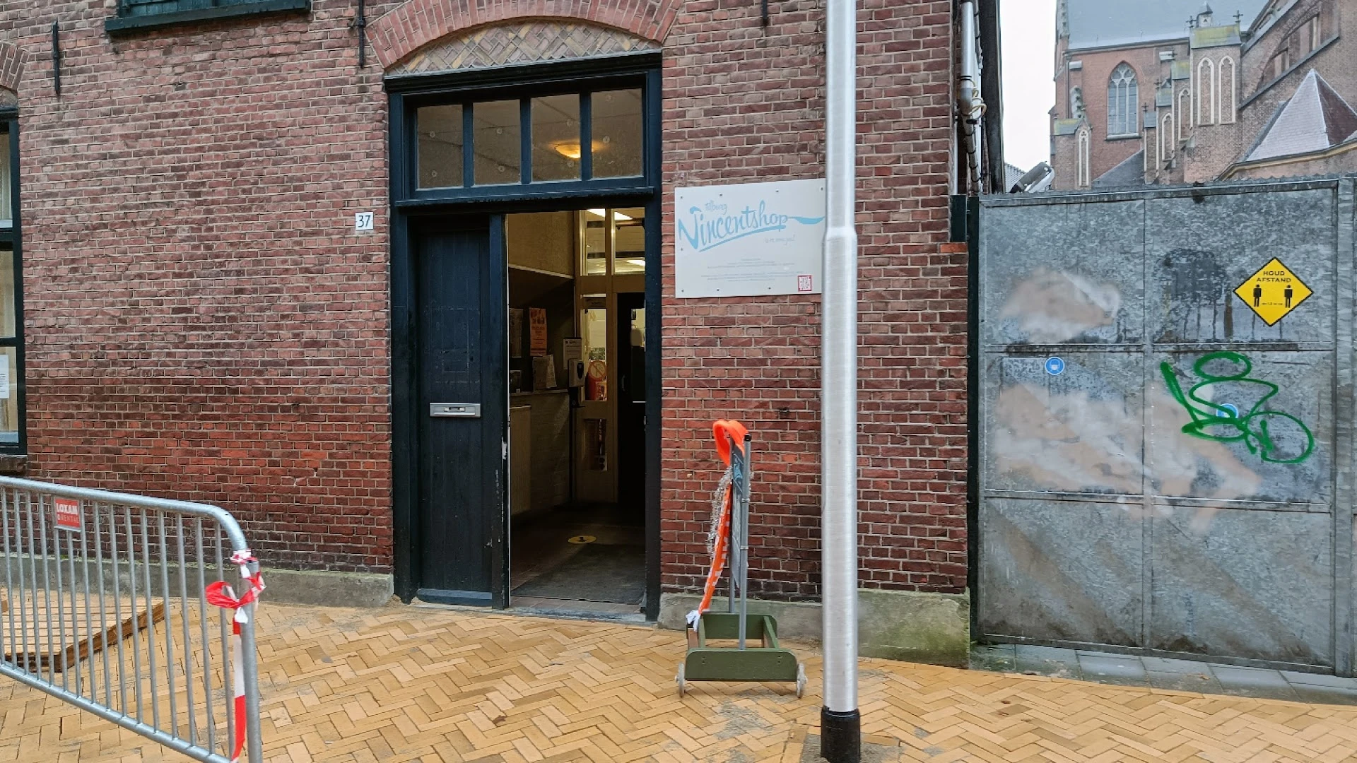 Voorgevel van kringloopwinkel met zwarte deur, ramen en bakstenen muur aan Ceramstraat