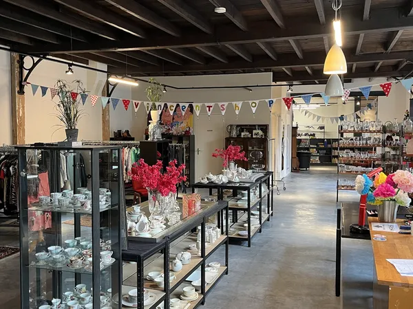 Ruim interieur van kringloopwinkel met zwarte stellingen vol huishoudelijke artikelen, decoraties en bloemen, festieve slinge