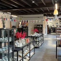 Ruim interieur van kringloopwinkel met zwarte stellingen vol huishoudelijke artikelen, decoraties en bloemen, festieve slinge