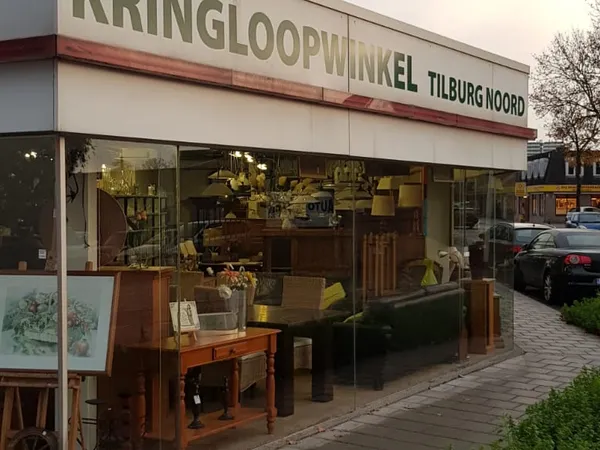 Gevel van Kringloopwinkel Tilburg Noord met grote ramen, winkelnaam zichtbaar, meubels in etalage