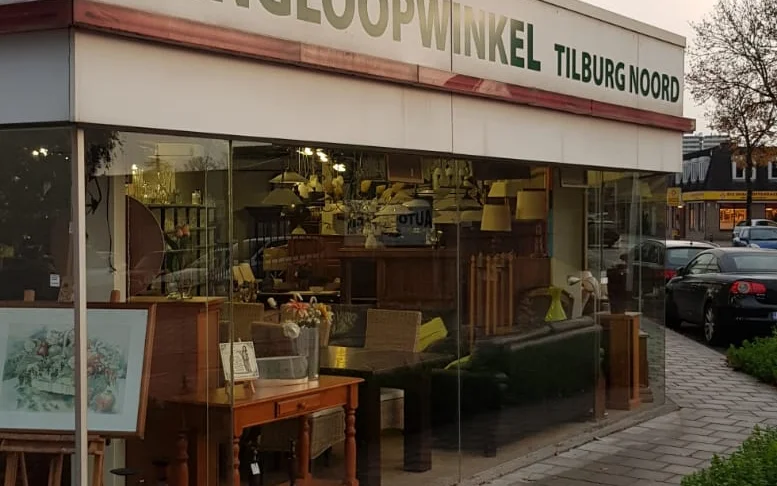 Gevel van kringloopwinkel Tilburg Noord met grote ramen waarachter meubelen en huishoudartikelen zichtbaar zijn