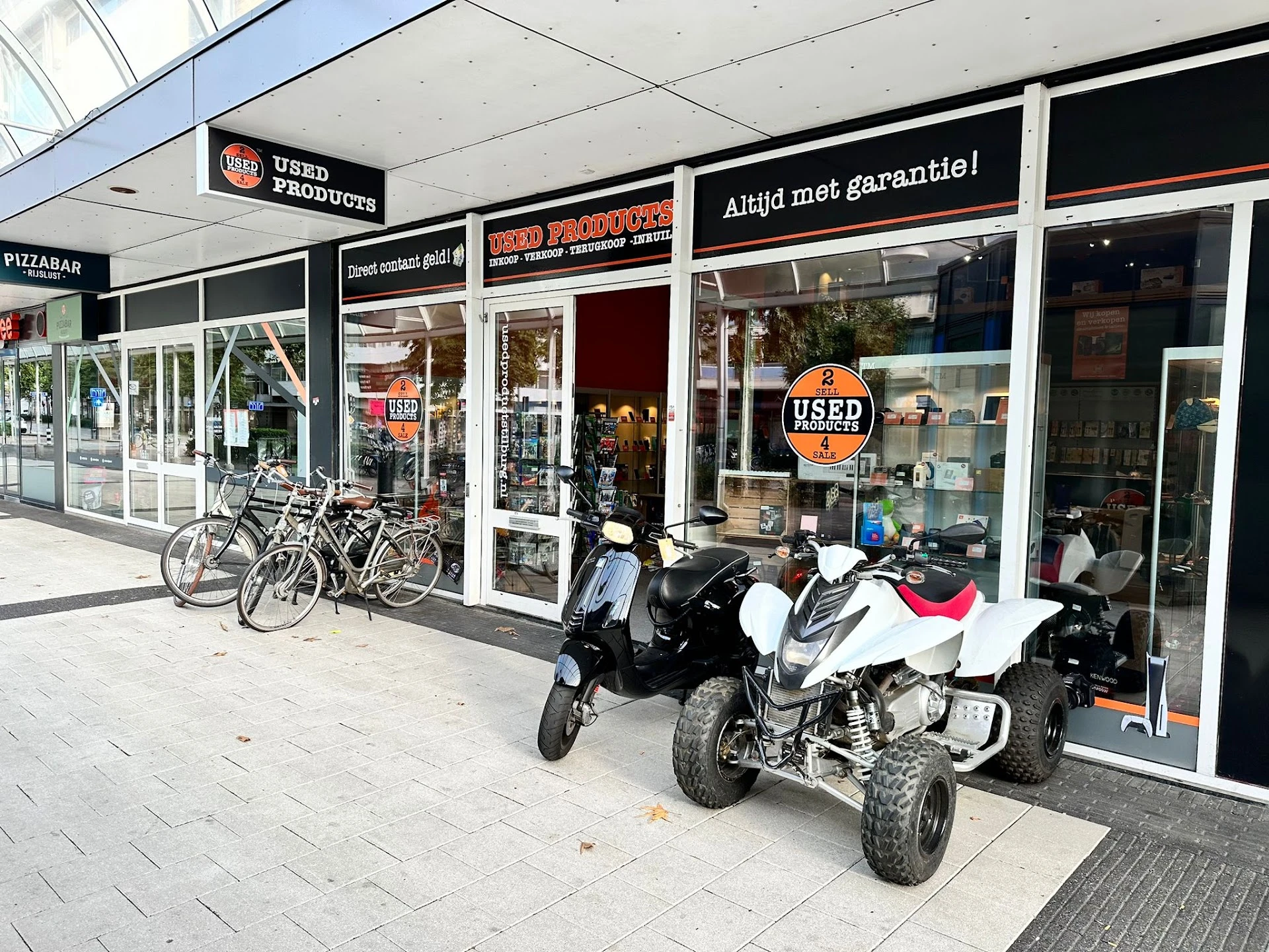 Winkelfront met etalage, fietsen en brommers geparkeerd ervoor op het terras