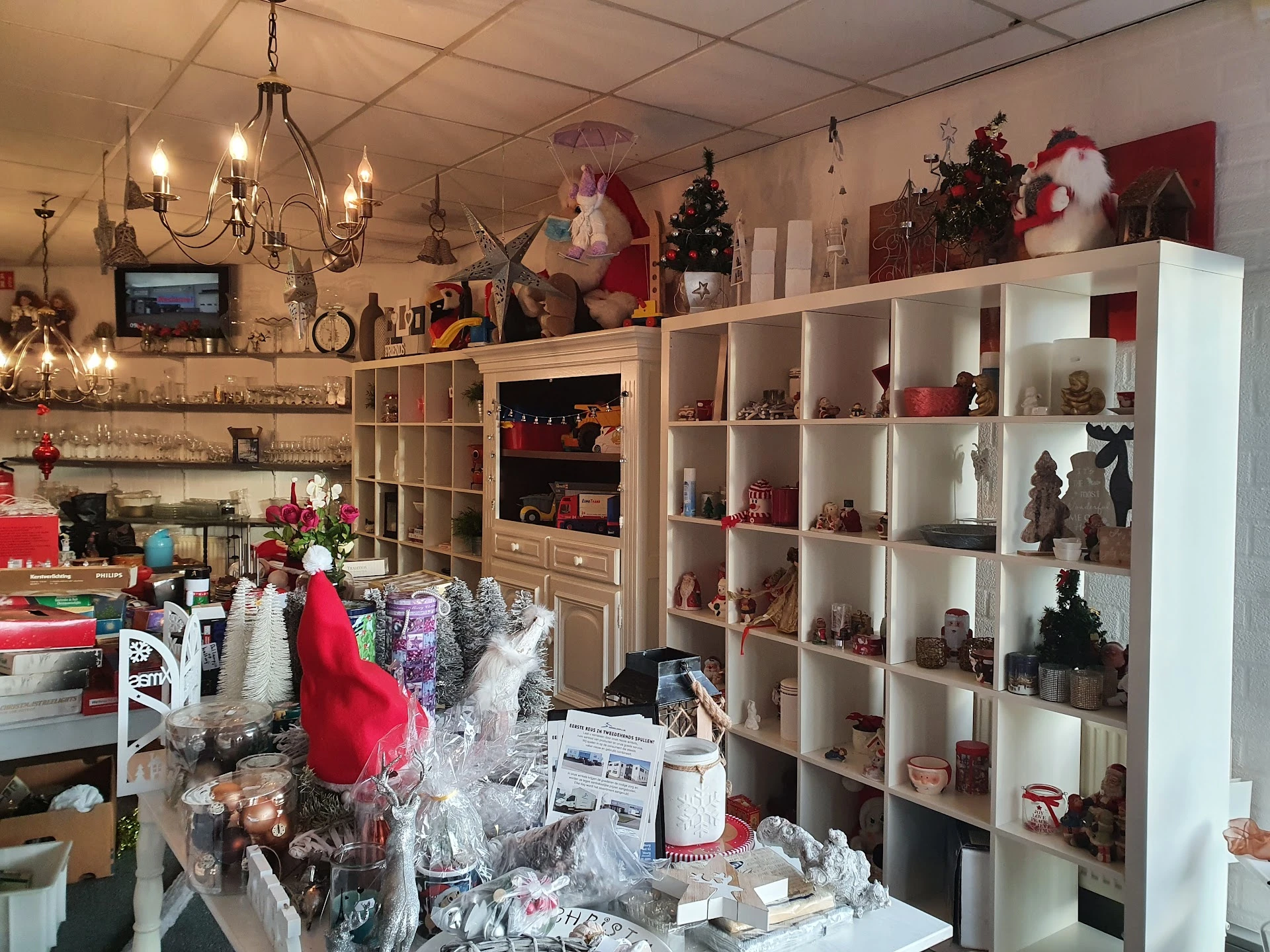 Winkelbinnenkant met witte stellingkasten vol decoratie en kerstversiering, kroonluchter en diverse items op tafels