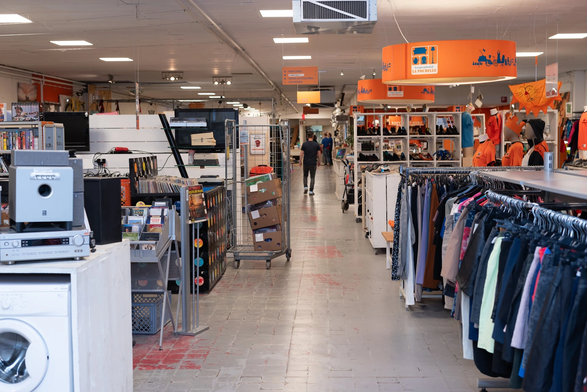 Winkelvloer van kringloopwinkel met rekken met kleding, huishoudapparaten en oranje display-elementen