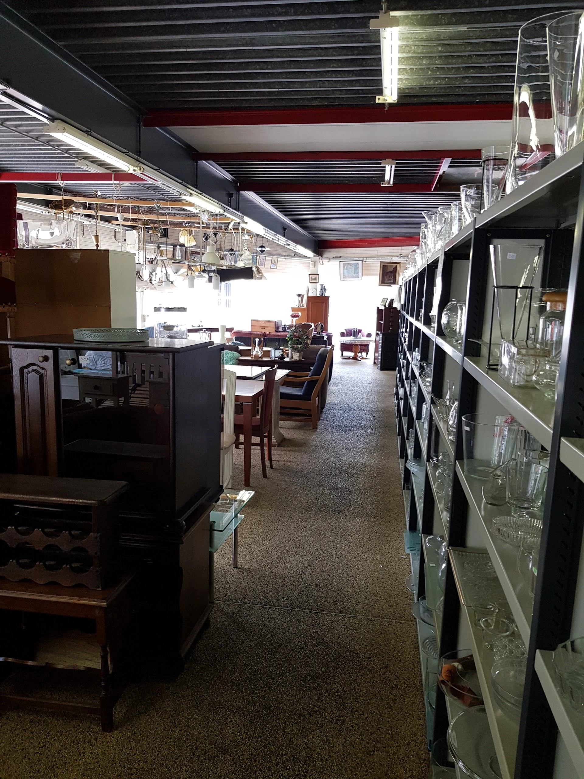 Winkelvloer van kringloopwinkel met rekken vol glaswerk, meubilair en huishoudartikelen