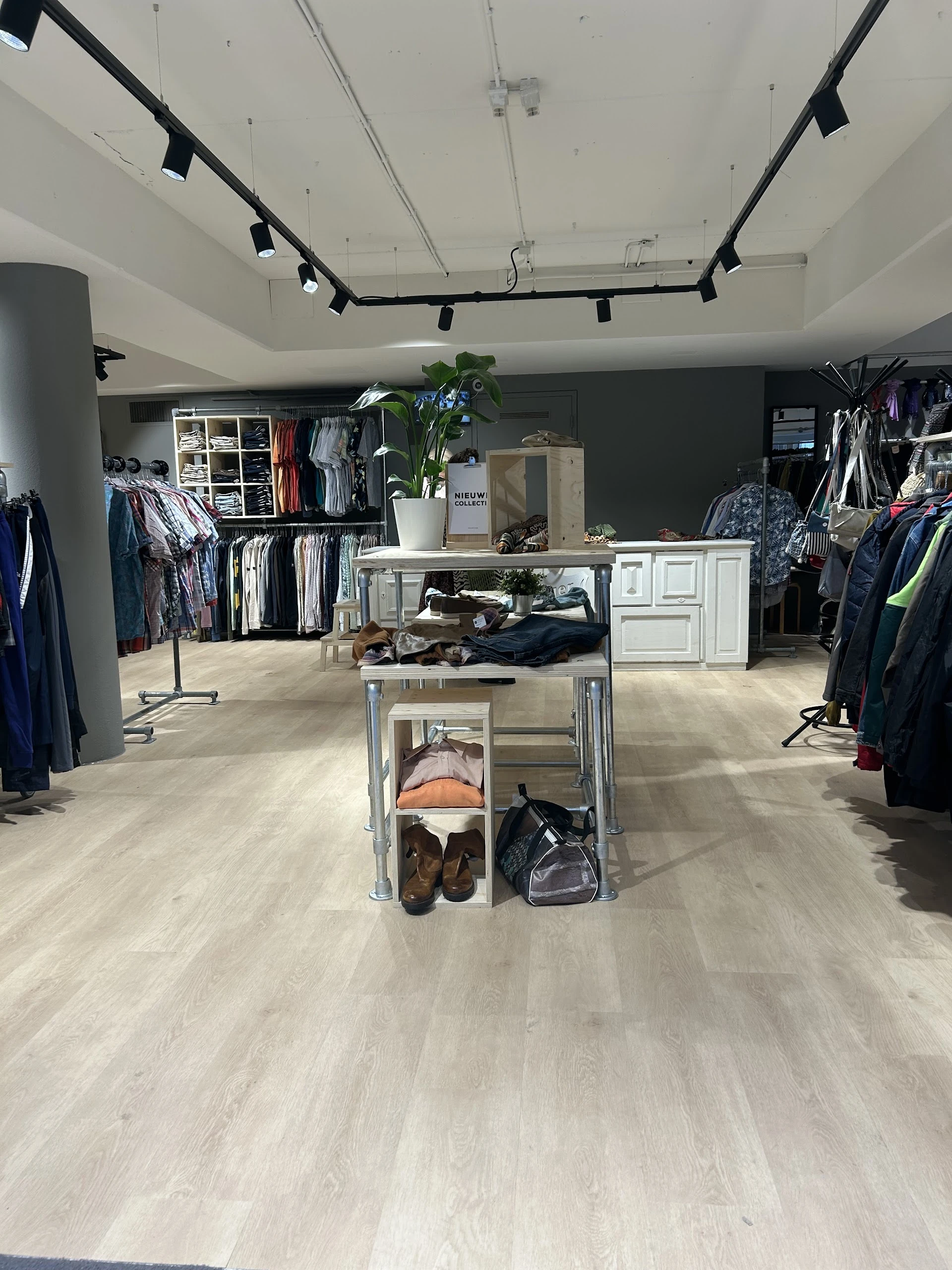 Ruime winkelruimte met kledingrekken, stellingen en een centrale display tafel met schoenen en accessoires