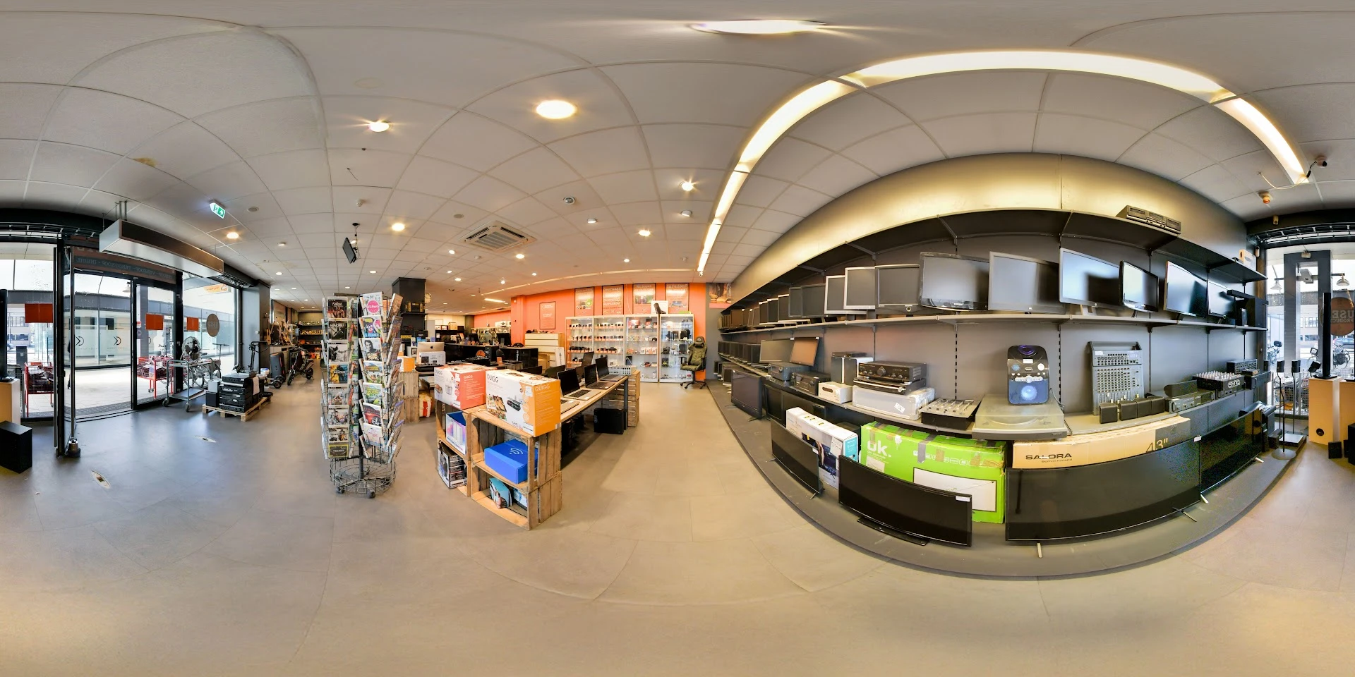 Panoramisch overzicht van kringloopwinkel met stellingen, displaykasten en diverse spullen verspreid over de winkelvloer