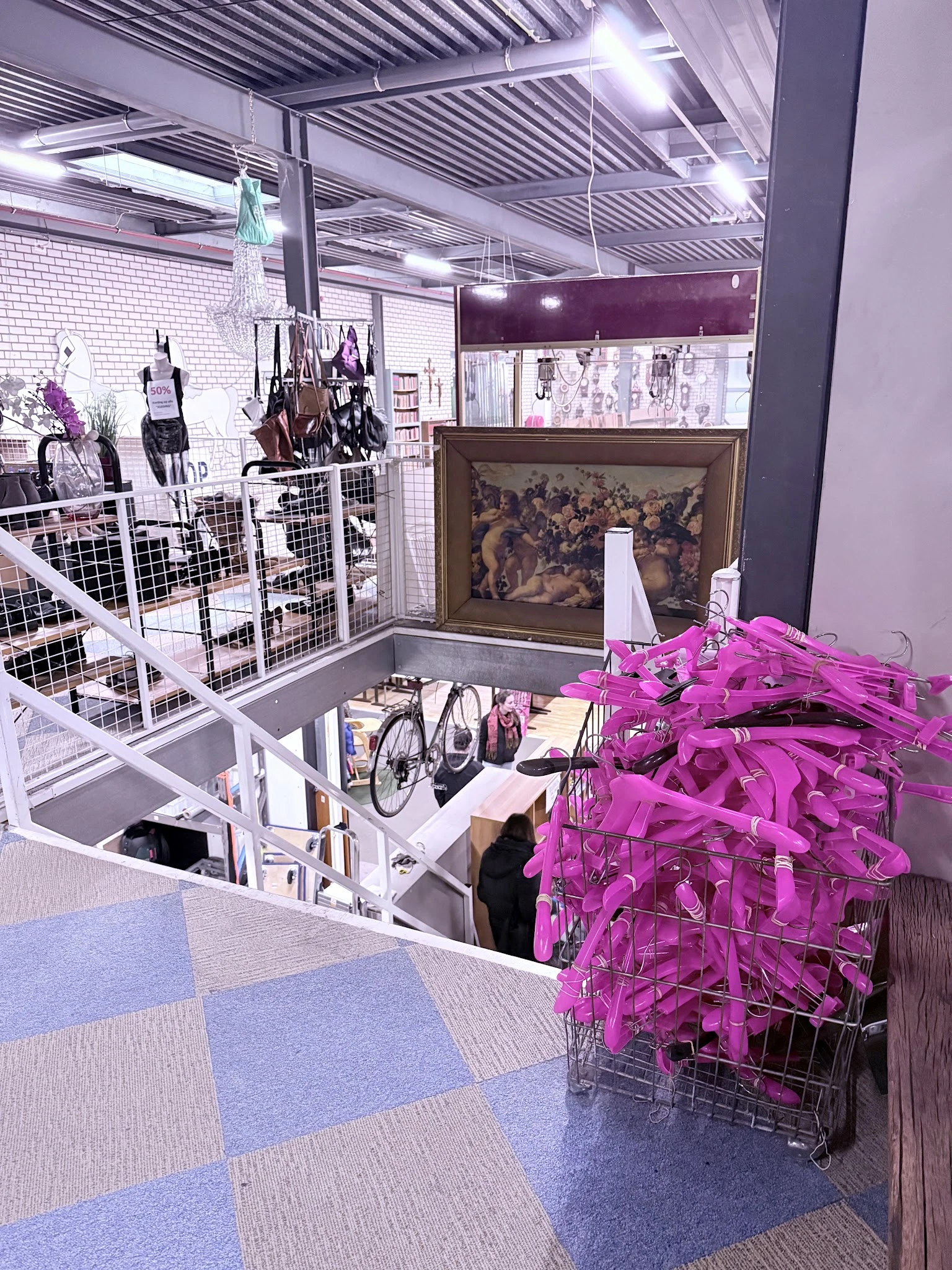 Winkelvloer van kringloopwinkel met stellingen, uitgestalde kleding op hangers en roze plastic kledinghaken op voorgrond