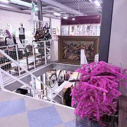 Winkelvloer van kringloopwinkel met stellingen, uitgestalde kleding op hangers en roze plastic kledinghaken op voorgrond