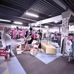 Winkelvloer met kledingrekken, mannequins en dozen in een kringloopwinkel met industrieel plafond