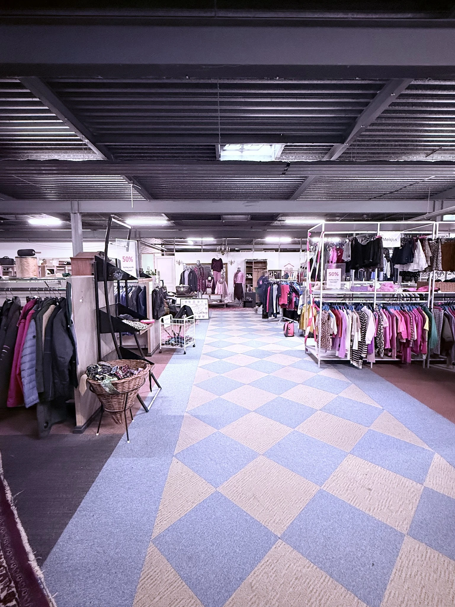 Ruim winkelinterieur met rekken vol tweedehands kleding in roze en zwarte tinten, diamantvormige vloer