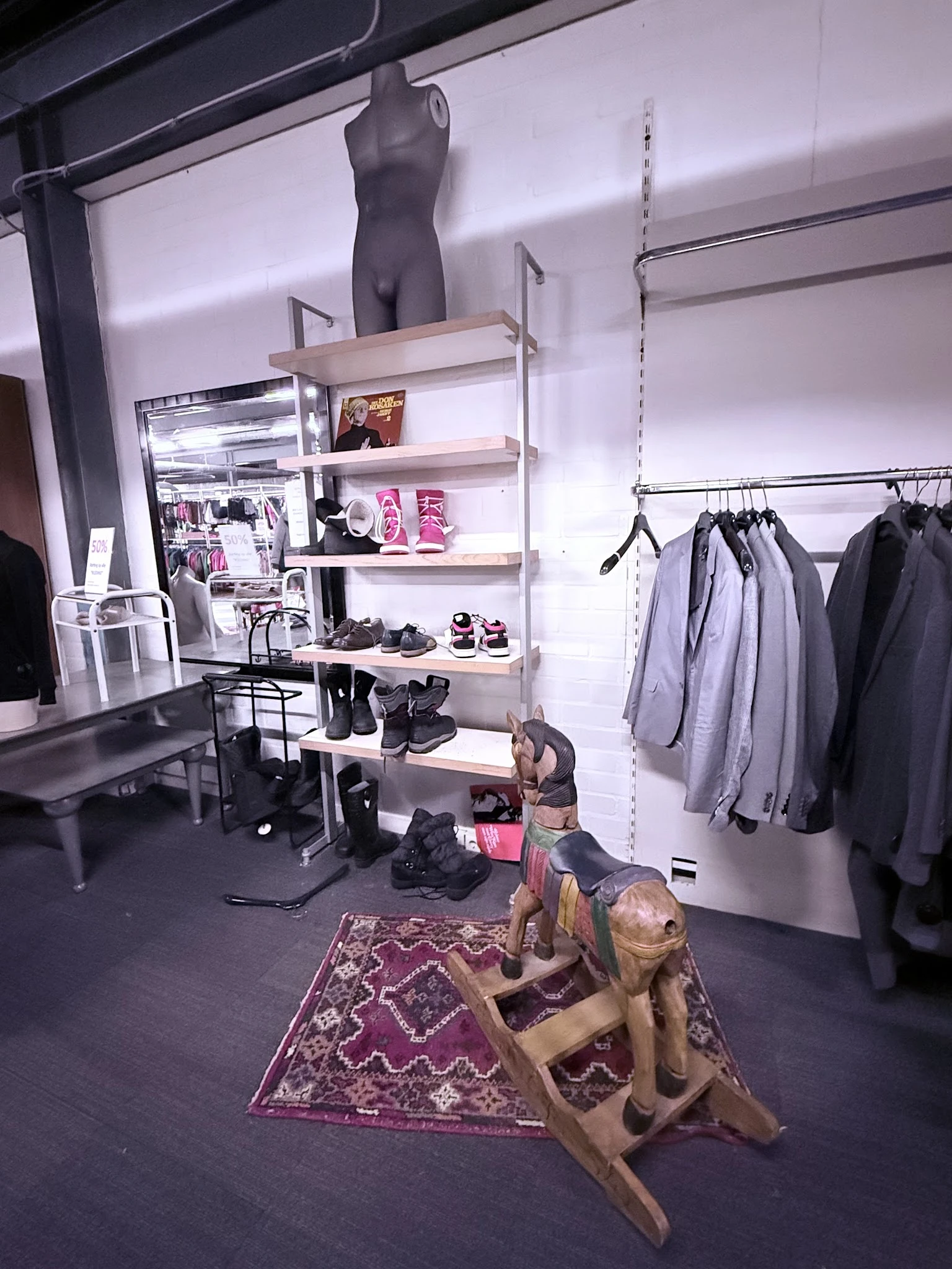Winkelbinnenruimte met kledingrekken, open stellingen met schoenen en accessoires, en een decoratief beeldje op het tapijt