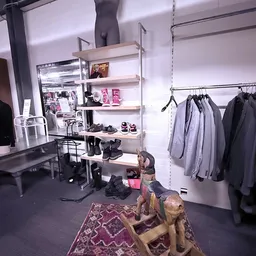 Winkelbinnenruimte met kledingrekken, open stellingen met schoenen en accessoires, en een decoratief beeldje op het tapijt