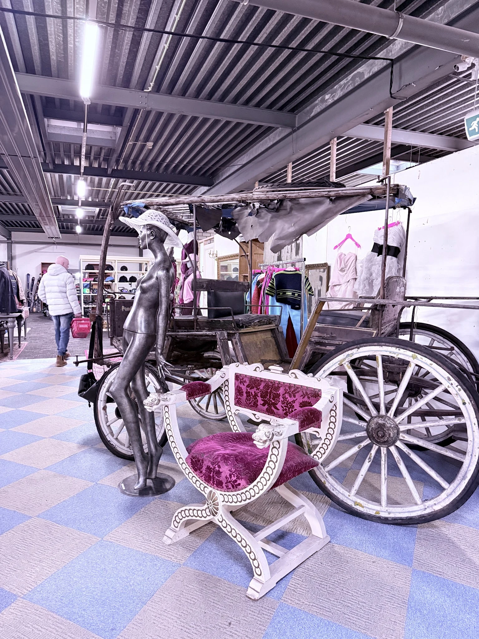 Winkelinterieur met een decoratieve zwarte paardenbeeldhouwwerk en een roze prinsessenwagen op wielen, omgeven door kledingre