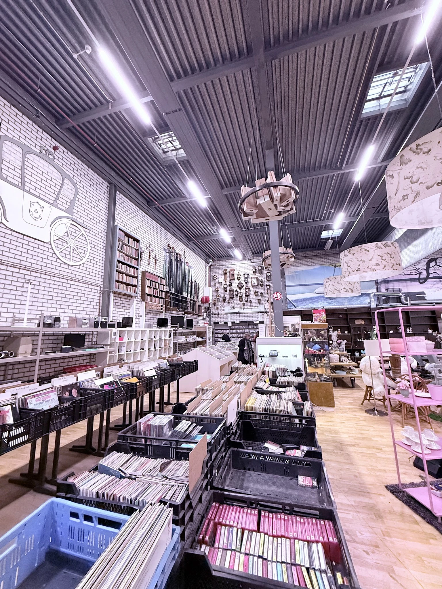 Overzicht van kringloopwinkel met stellingen, display-items, zwarte bakken met spullen en verlichting aan het plafond