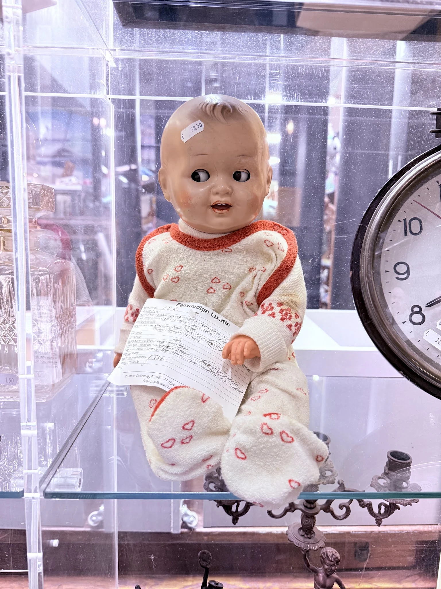 Vintage pop met wit-rood jurkje en hartjes-motief in vitrine, naast klok