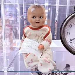 Vintage pop met wit-rood jurkje en hartjes-motief in vitrine, naast klok