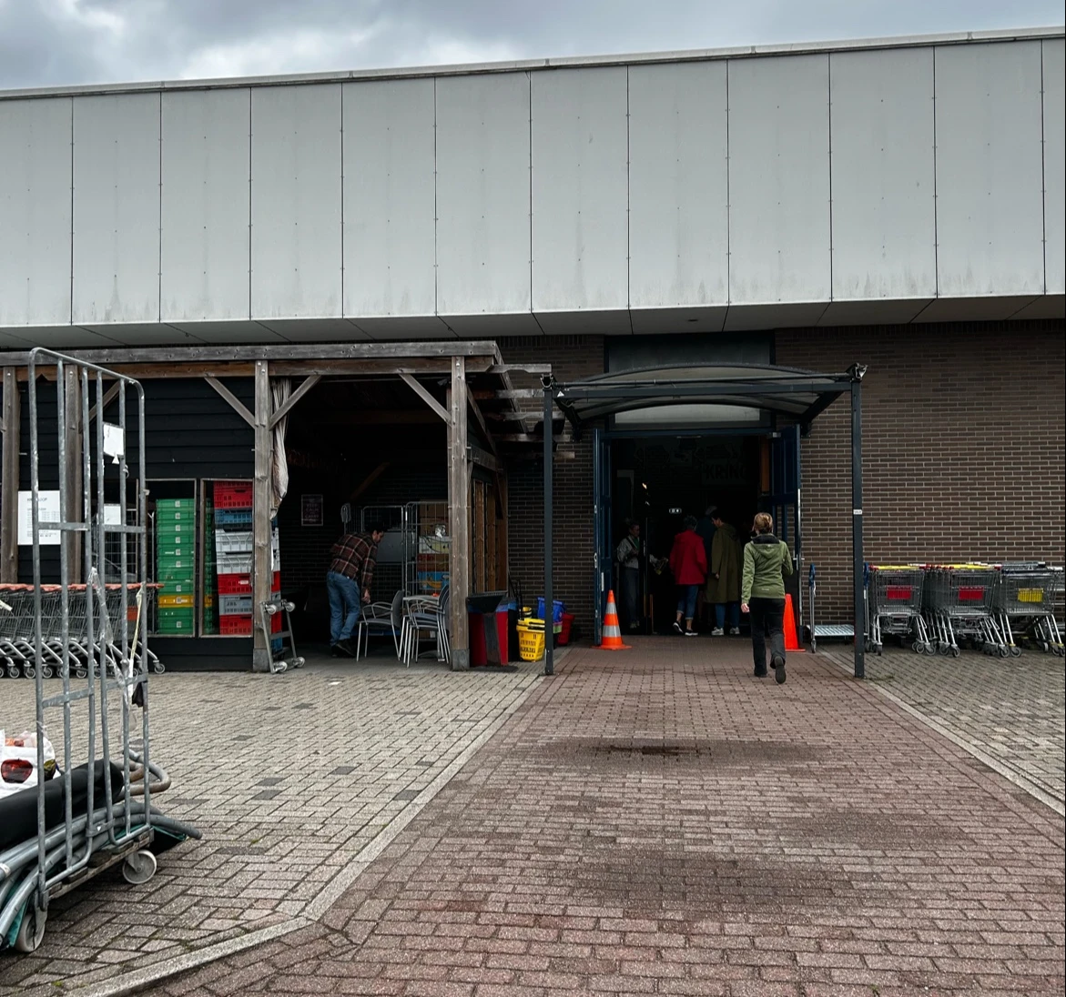 Voorkant van kringloopwinkel met ingang, deels verborgen door steigers en voorwerpen
