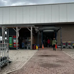 Voorkant van kringloopwinkel met ingang, deels verborgen door steigers en voorwerpen