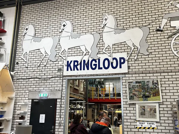 Witte bakstenen gevel met drie witte paardenbeelden en blauwe KRINGLOOP-letters boven de ingang
