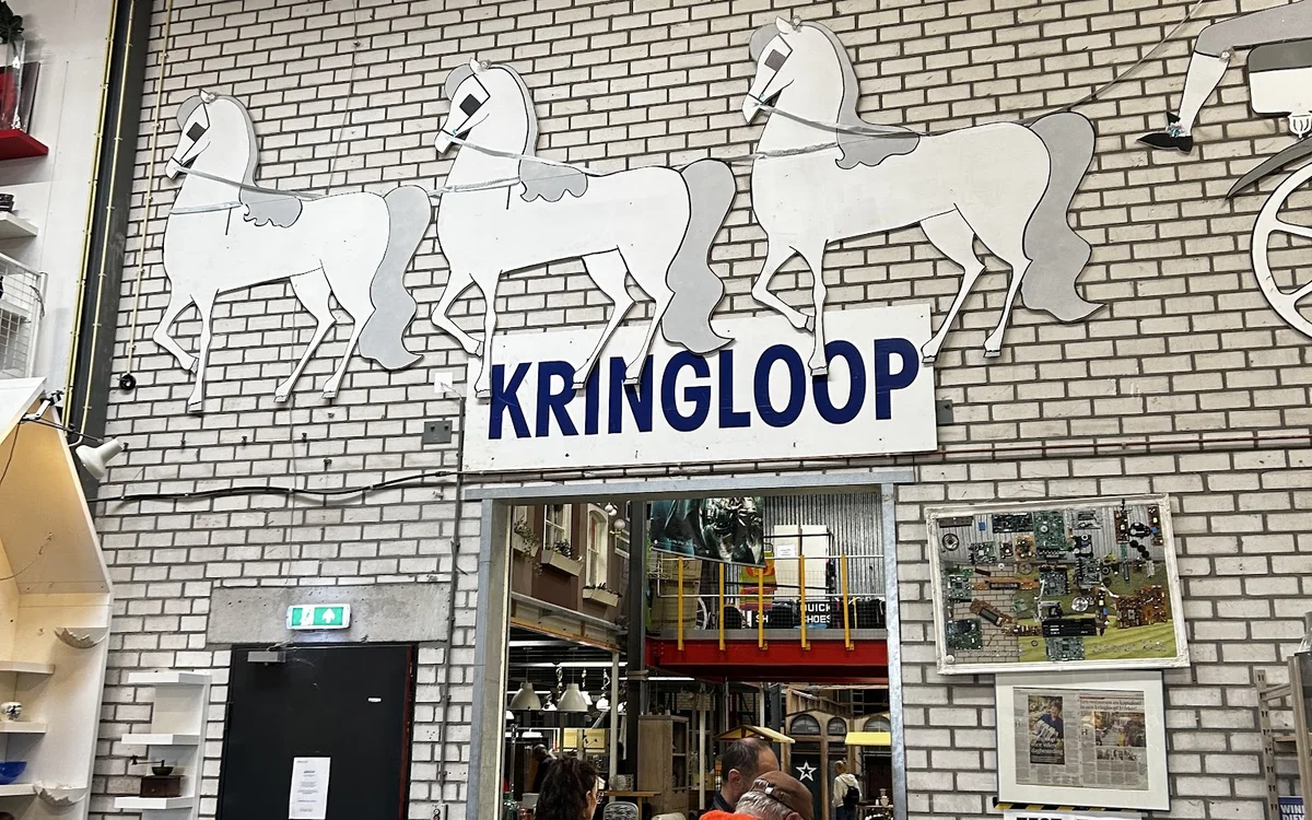 Witte bakstenen gevel met drie witte paardenbeelden en blauwe KRINGLOOP-letters boven de ingang