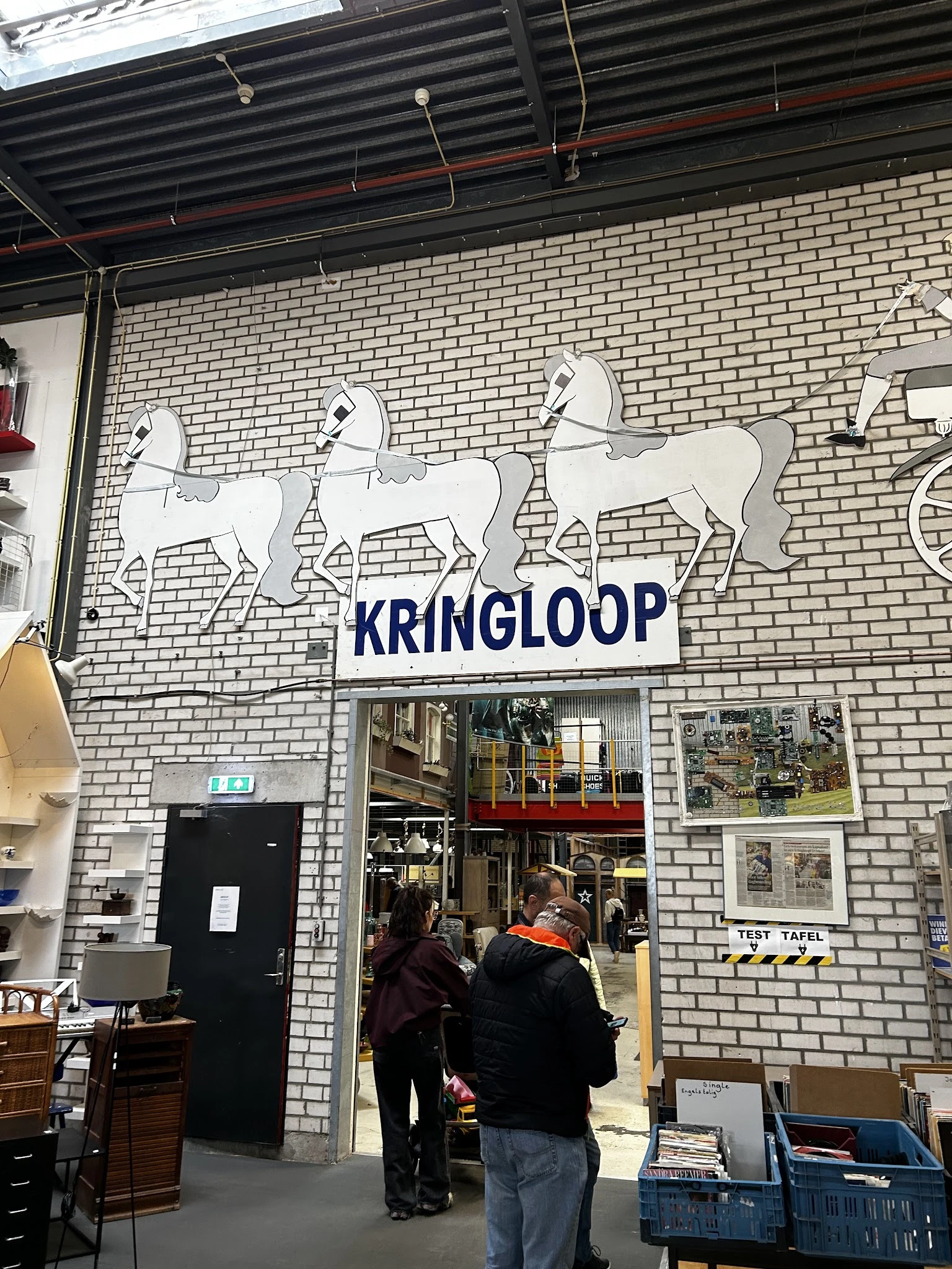 Witte bakstenen gevel met drie witte paardenbeelden en blauwe KRINGLOOP-letters boven de ingang