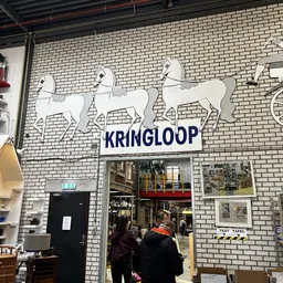 Witte bakstenen gevel met drie witte paardenbeelden en blauwe KRINGLOOP-letters boven de ingang