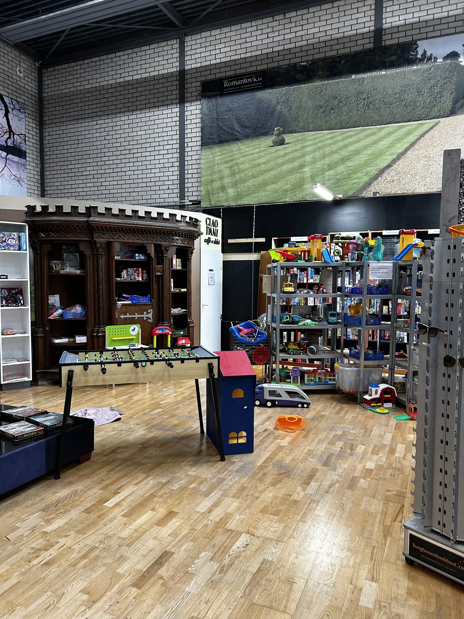 Winkelvloer met foosballtafel, speelgoedkasteel, stellingen met speelgoed en boeken tegen de wand, groen grasveld zichtbaar o