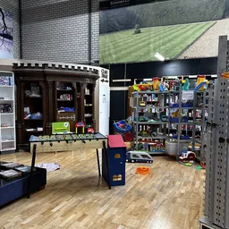 Winkelvloer met foosballtafel, speelgoedkasteel, stellingen met speelgoed en boeken tegen de wand, groen grasveld zichtbaar o
