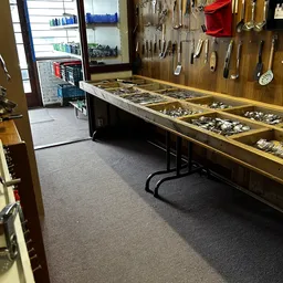 Kringloopwinkel met lange vitrinekast vol serviesgoed en bestek, gereedschappen aan muur, overzicht van winkelruimte