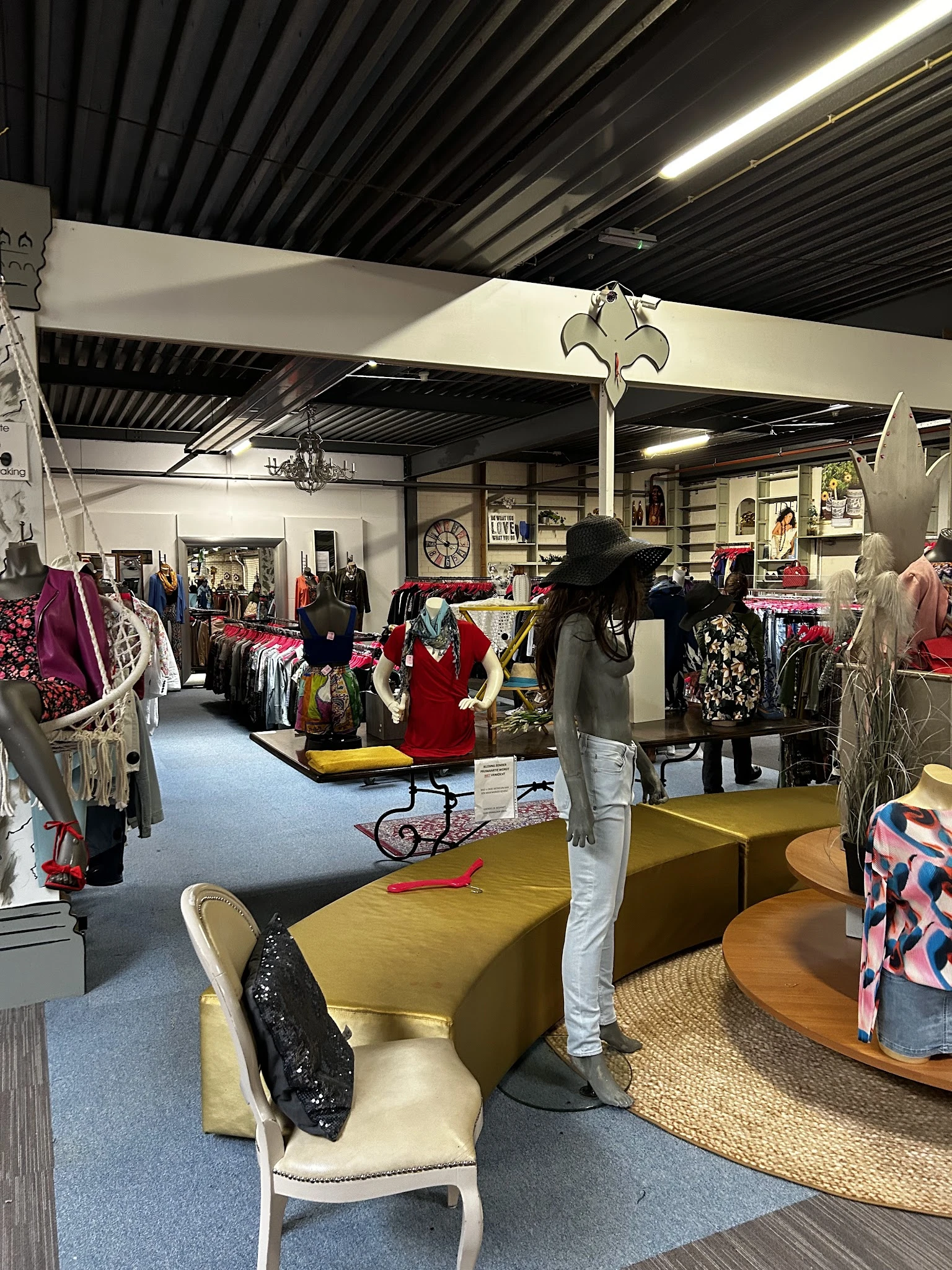 Winkelinterieur met kledingrekken, mannequins en diverse tweedehands artikelen op verschillende afdelingen