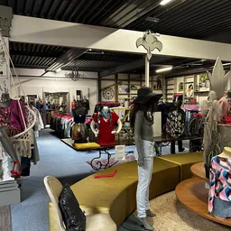 Winkelinterieur met kledingrekken, mannequins en diverse tweedehands artikelen op verschillende afdelingen