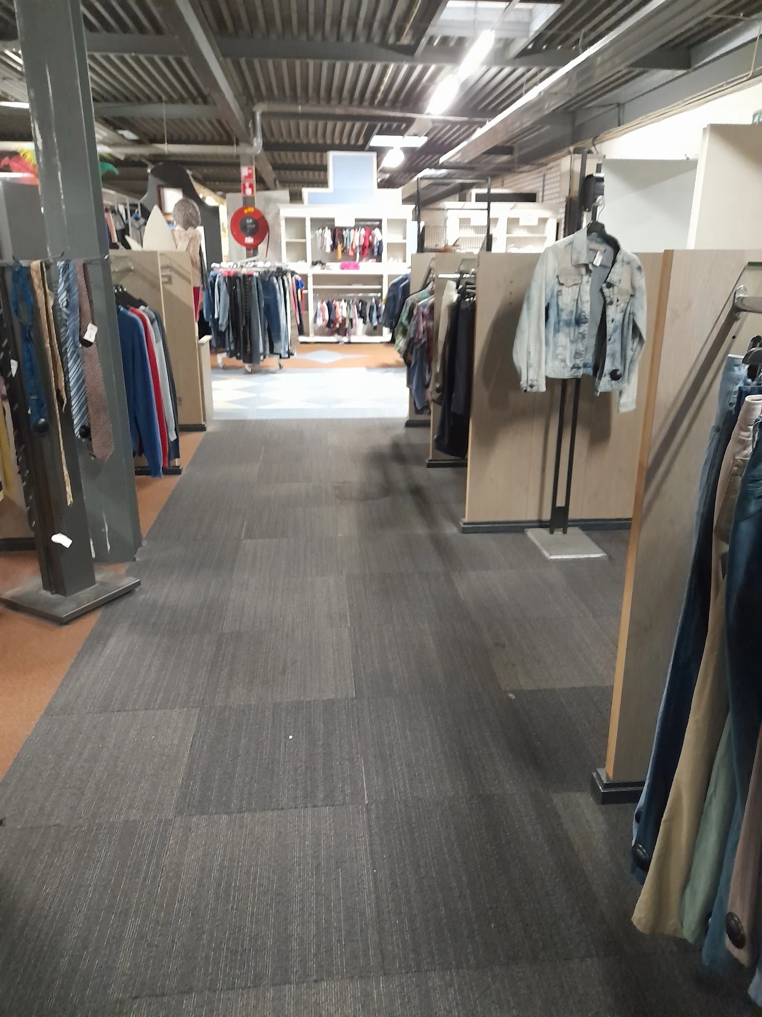 Winkelinterieur met kledingrekken aan beide zijden van een gang met grijze vloer