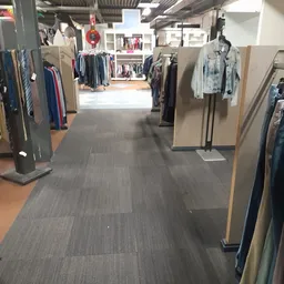 Winkelinterieur met kledingrekken aan beide zijden van een gang met grijze vloer