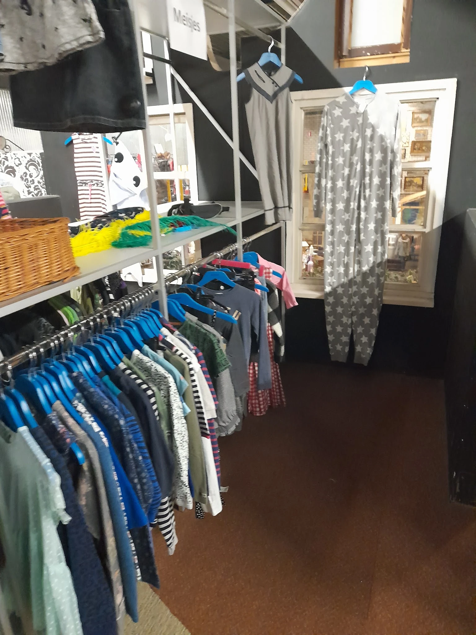 Rekken met tweedehands kleding in verschillende kleuren en maten, met op de achtergrond stellingen met gefolde kledingstukken