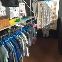 Rekken met tweedehands kleding in verschillende kleuren en maten, met op de achtergrond stellingen met gefolde kledingstukken