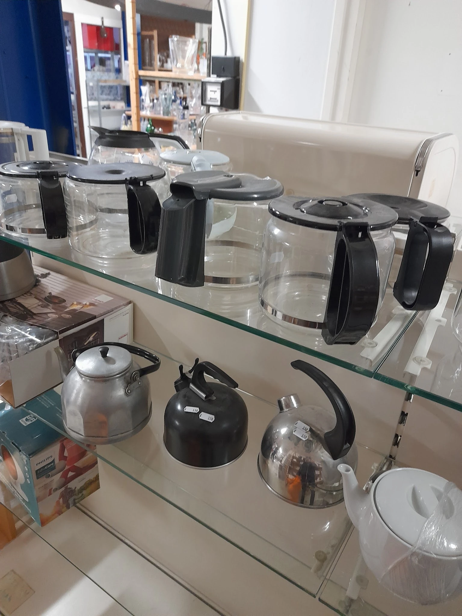 Glazen plankje met koffiezetapparaten en waterkannen op display in kringloopwinkel