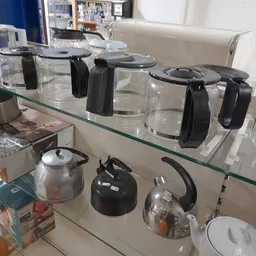 Glazen plankje met koffiezetapparaten en waterkannen op display in kringloopwinkel