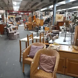Winkelvloer van kringloopwinkel met rieten stoelen, houten tafels en diverse meubels op de achtergrond