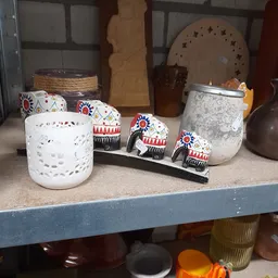 Uitgestalde decoratieve items op een plank: witte kandelaar, grijze pot en drie beschilderde olifantjes met etnische patronen